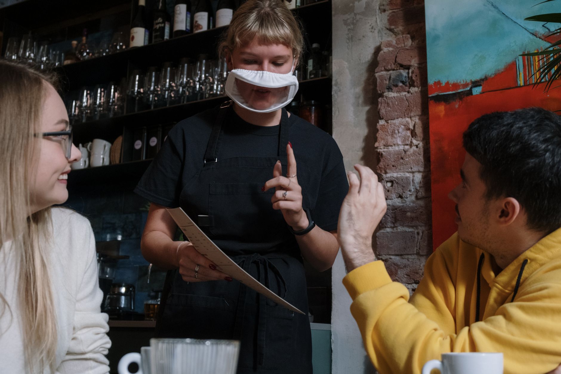 A waitress using sign language to take an order from customers in a modern cafe.