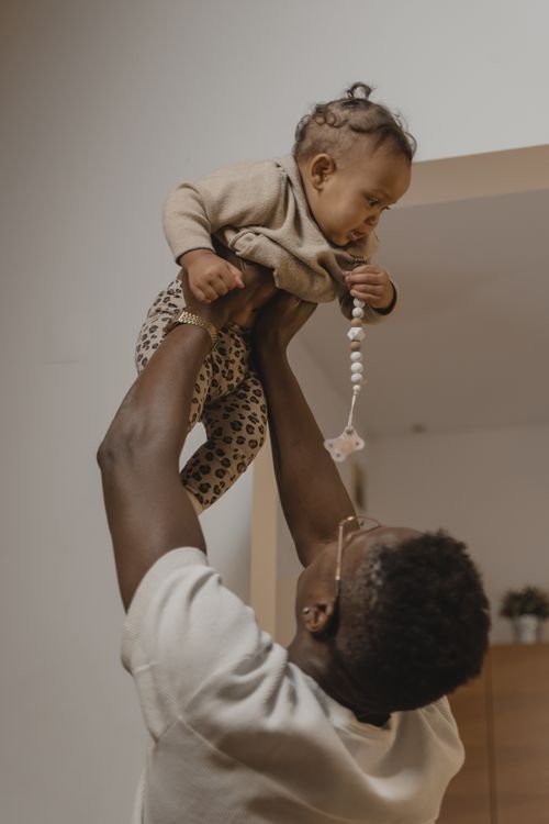 Free A joyful father lifting his baby in an indoor setting, creating a heartwarming moment. Stock Photo