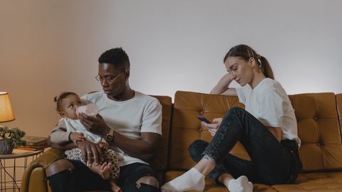 Family enjoying a relaxing moment on the couch, feeding a toddler in a cozy living room.