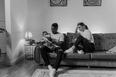 Monochrome image of a family with a father feeding a baby while sitting on a sofa.