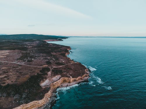 Aerial view of roadway on mount with trees against foamy ocean under cloudy sky in cold weather