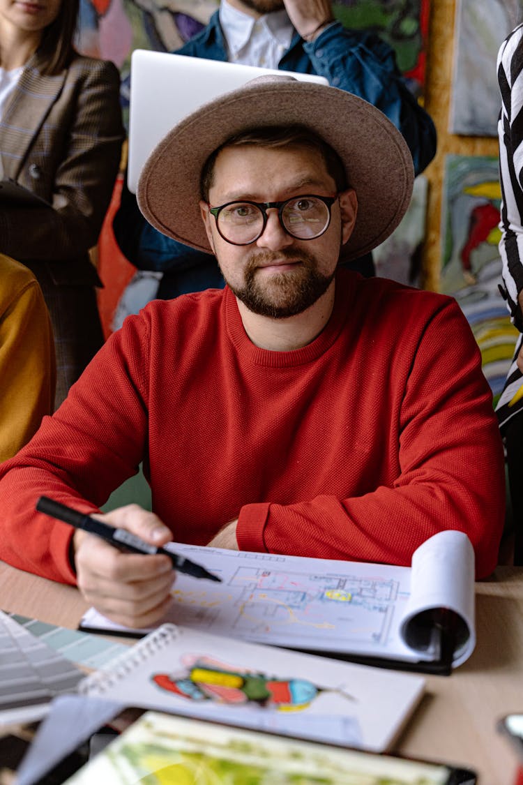 Man In A Hat And Red Sweatshirt Drawing In Sketchbook