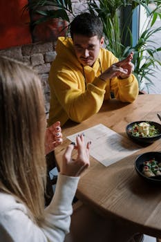 Two friends communicate using sign language at a restaurant table with salads.
