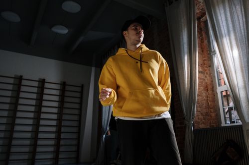 Free Man in yellow hoodie dancing indoors with dramatic lighting and shadows. Stock Photo