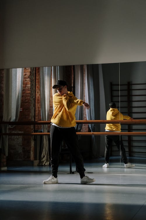 A Man in Yellow Hoodie Stretching His Arms while Standing in the Dance Studio