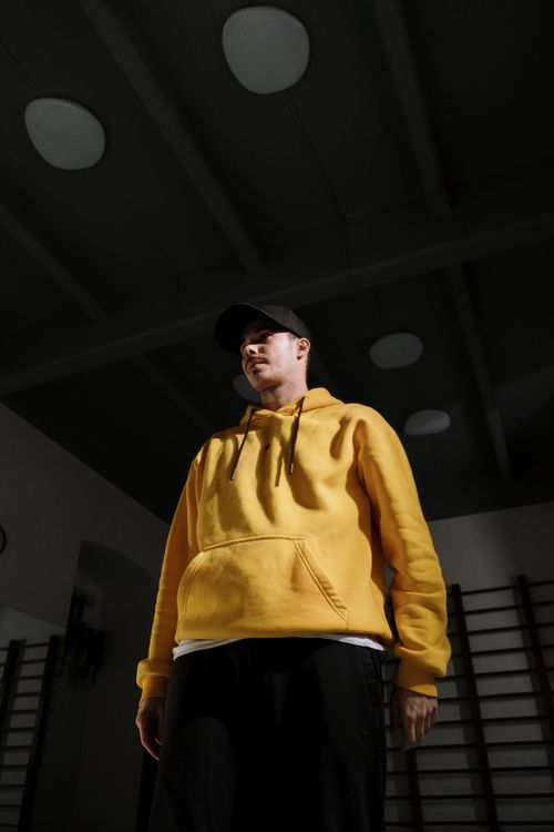 Free A stylish man in a yellow hoodie and cap standing in a modern interior. Stock Photo