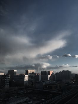 Picturesque aerial view of city district with various high residential houses near building crane under partly cloudy sky in daytime