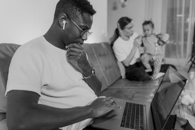 A Man Using Laptop Sitting On Couch Near A Woman Holding Holding A Baby