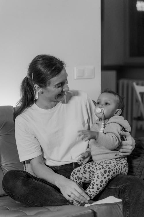 Grayscale  Photo of a Woman Sitting on Chair Holding a Baby with Pacifier