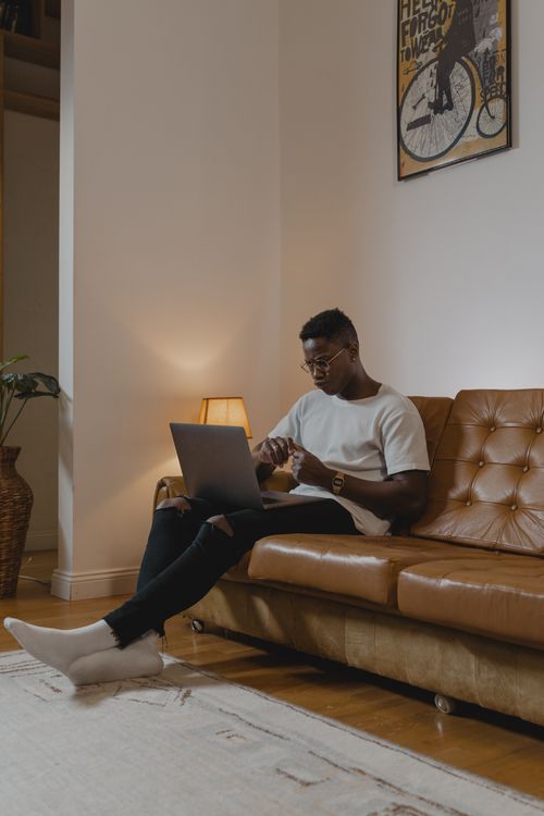 Free A man sitting on a leather couch using a laptop in a cozy indoor setting, creating a relaxed atmosphere. Stock Photo