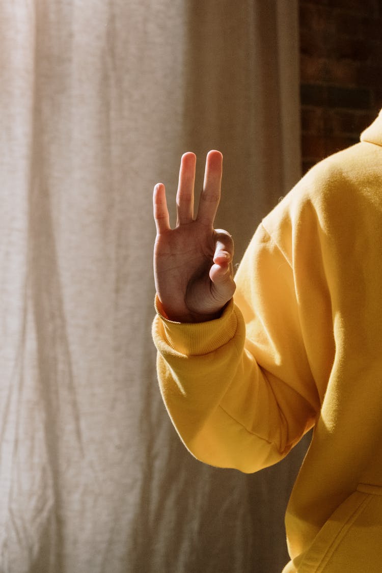 A Person In Yellow Hoodie Doing Hand Sign
