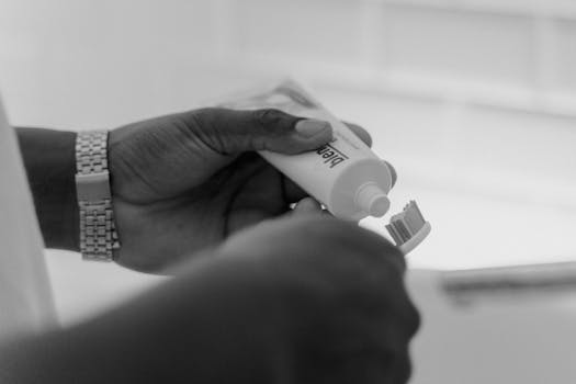 Monochrome close-up of hands applying toothpaste onto a toothbrush.