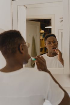 An adult man brushes his teeth in front of a bathroom mirror, emphasizing oral hygiene.