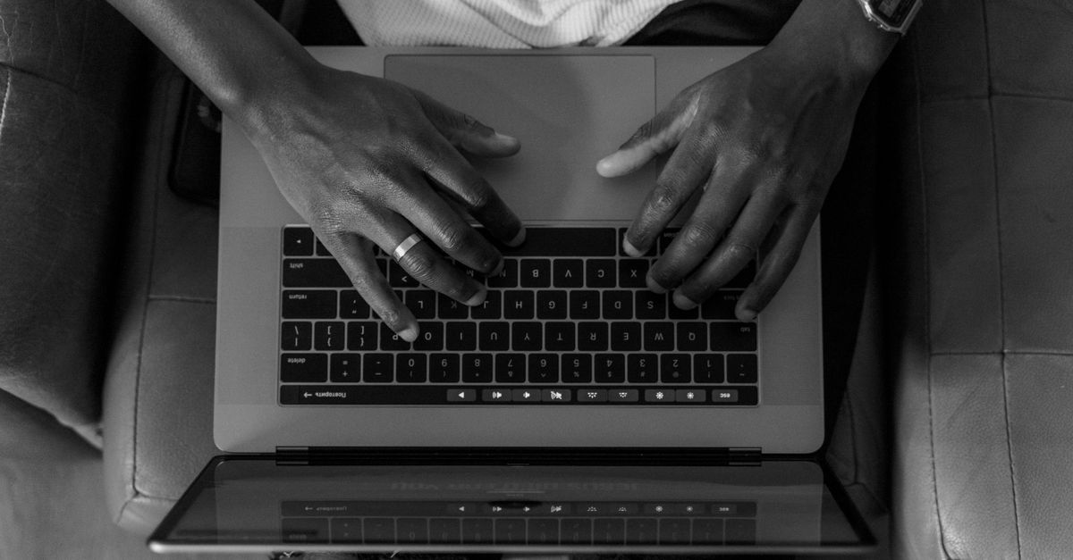 A black and white photo of hands typing on a laptop from an overhead perspective, conveying focus.