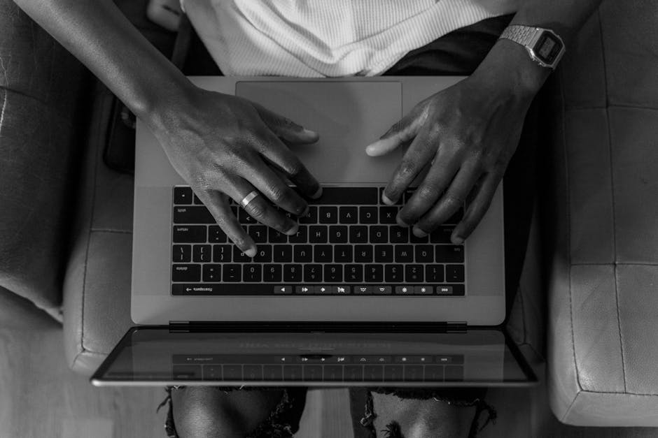 Credit Karma vs Experian: Score Accuracy Showdown A black and white photo of hands typing on a laptop from an overhead perspective, conveying focus.