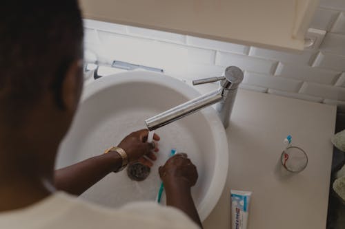 A Person Washing His Hand and the Toothbrush he is Holding on the Sink