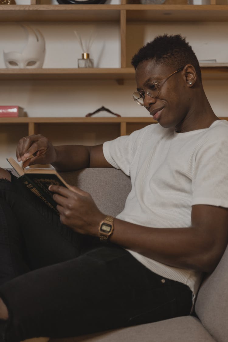 A Man In White Shirt Sitting On A Couch While Reading A Book