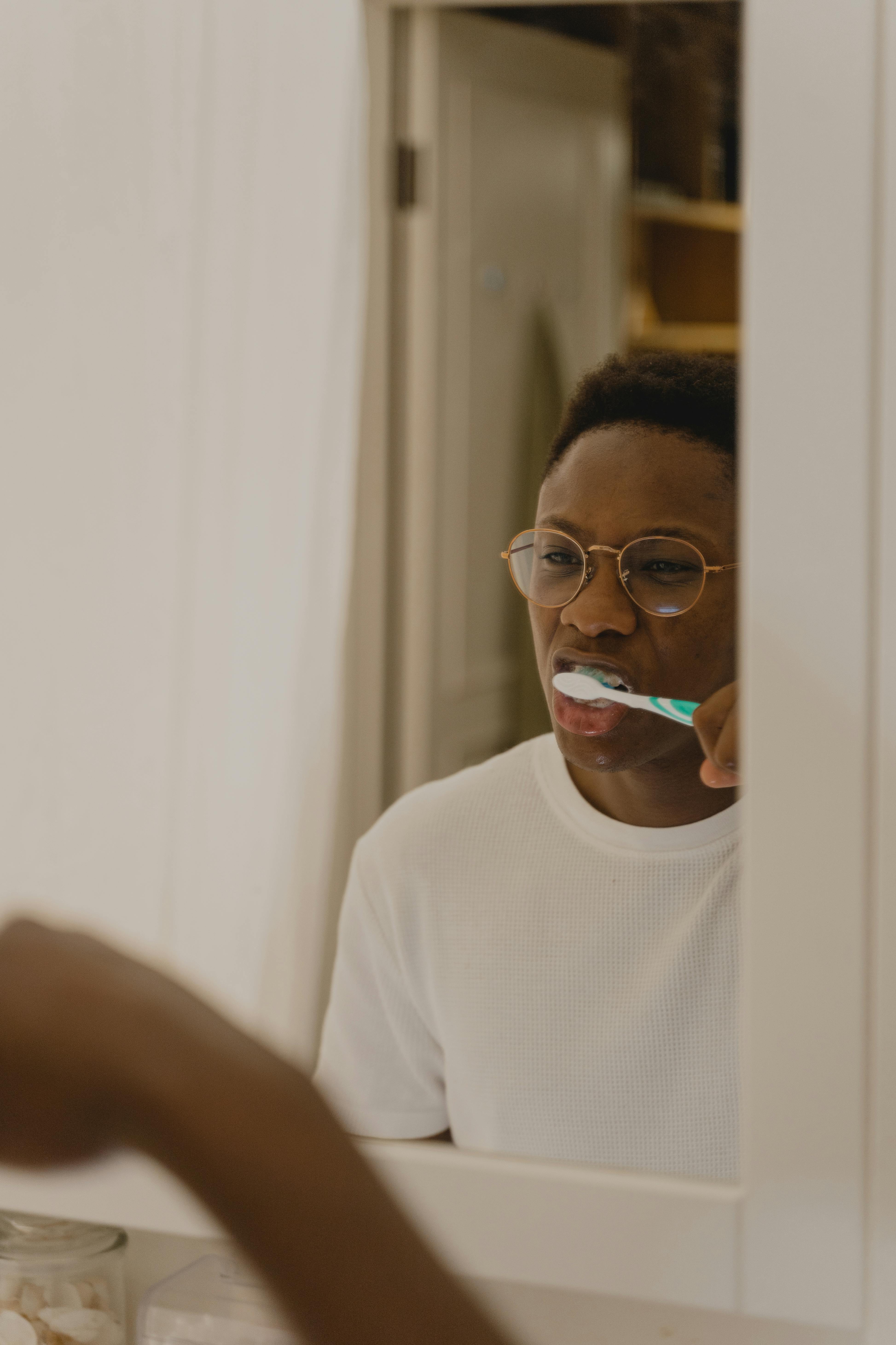 African American man brushing teeth in front of a bathroom mirror.