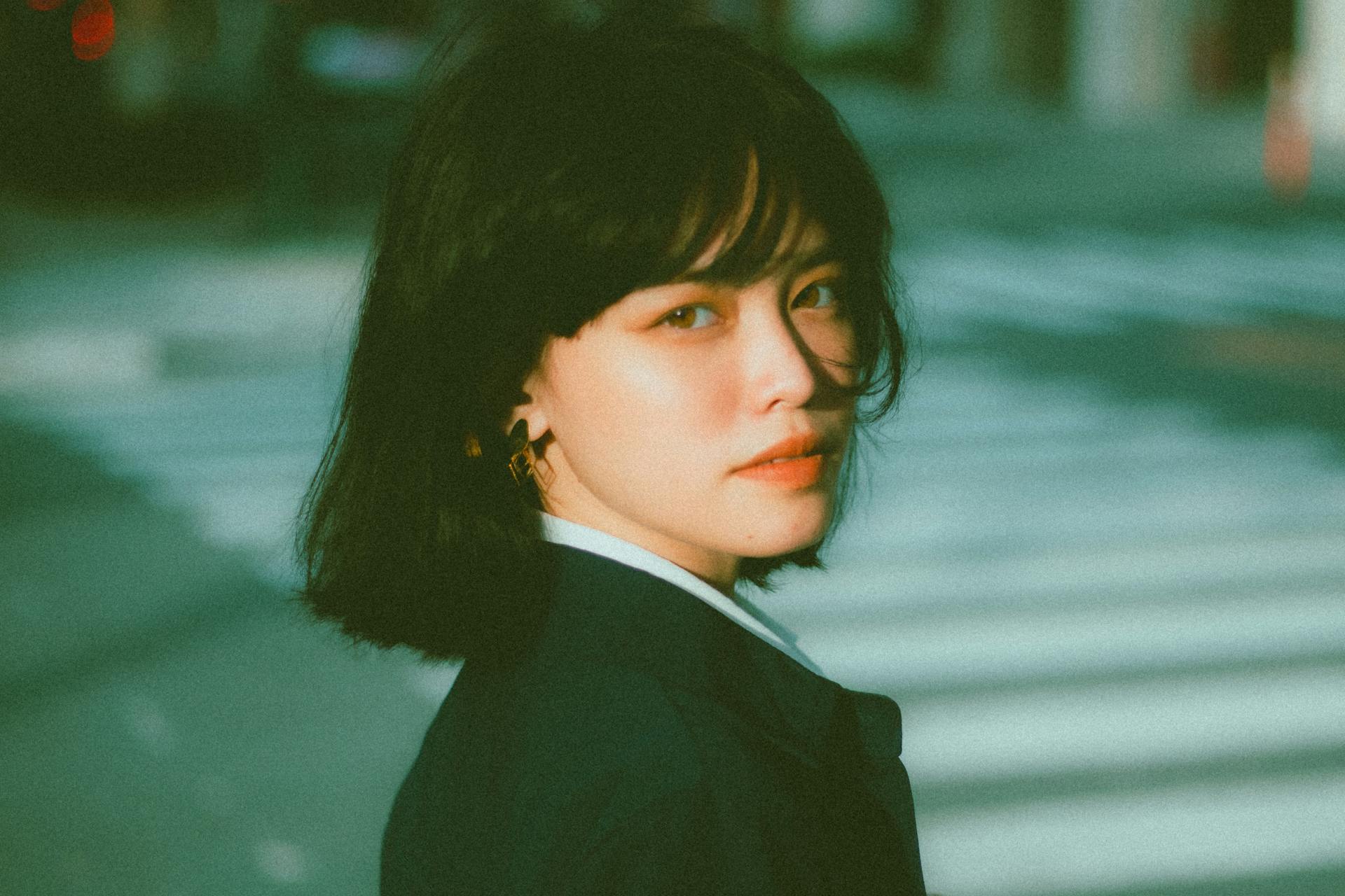 Side view of confident young Asian female entrepreneur in elegant outfit standing on city street and looking at camera