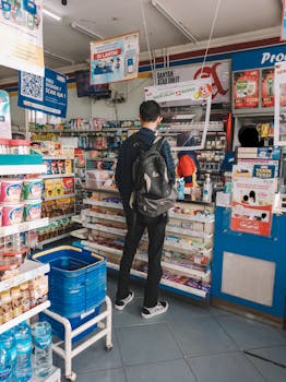 A man with a backpack shops at a convenience store counter filled with various products.