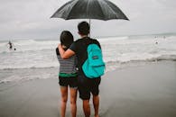 一对夫妇撑着伞，在多雨的海滩上拥抱，欣赏海景