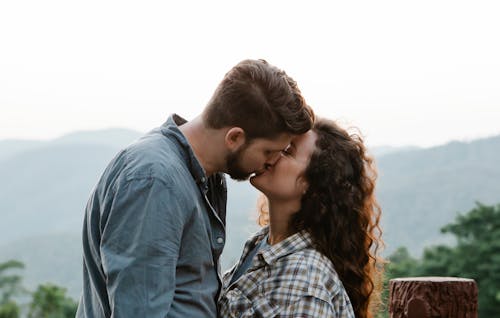 Free Side view of young loving couple in casual outfits kissing each other during romantic date in mountainous countryside Stock Photo
