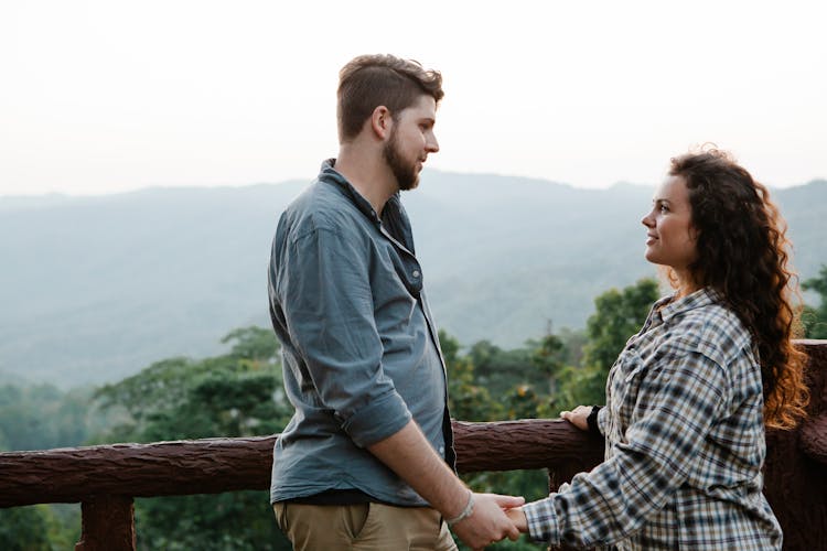 Romantic Young Couple Holding Hands While Resting On Terrace In Mountainous Valley