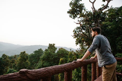 Pensive young guy enjoying mountain view from wooden terrace