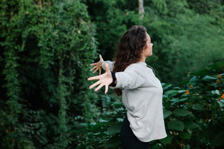 Woman standing with arms outstretched among lush green foliage