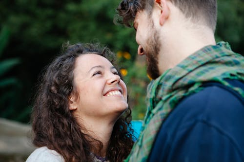 Cheerful girlfriend smiling and looking at happy crop anonymous boyfriend on blurred background of verdant forest