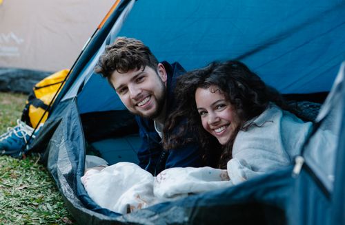 Free Young delighted couple smiling and looking at camera on picnic in tent on green fresh grass Stock Photo