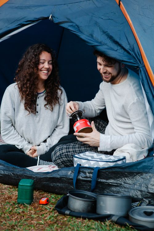 Free Cheerful young couple in pyjamas sitting in camping tent and having breakfast while spending holidays together in nature Stock Photo