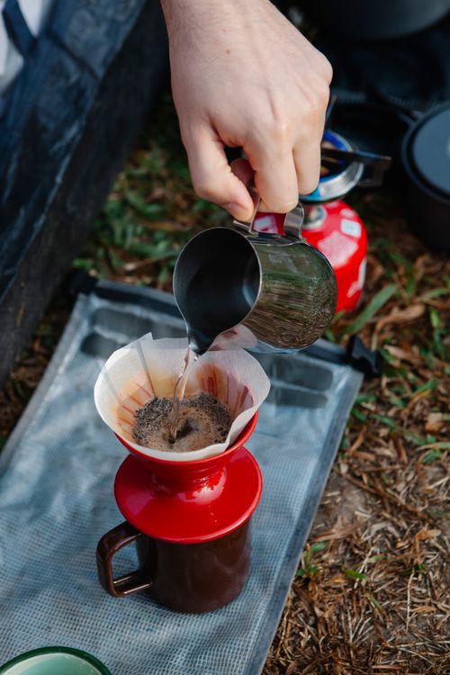 Free High angle of crop anonymous hiker pouring hot water from pitcher into filter with coffee while preparing hot drink Stock Photo