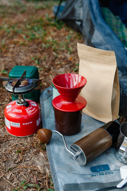 From above of drip coffee maker near package and portable gas bottle with burner stove on textile