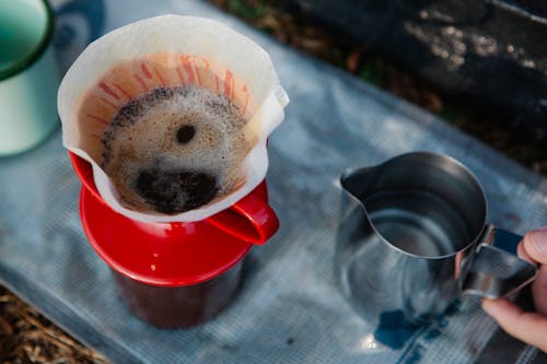 Crop hiker preparing coffee in carafe on fabric