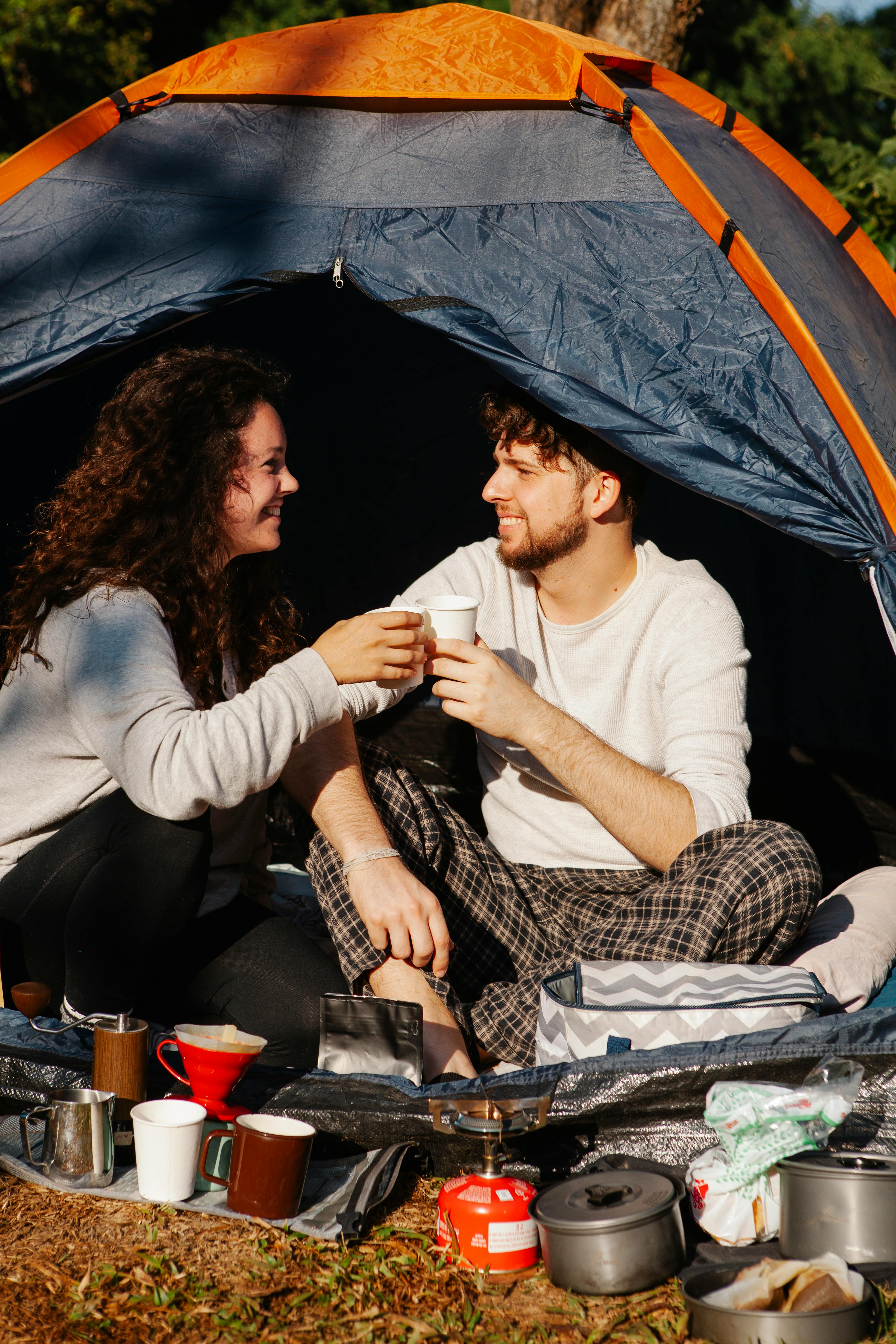 cheerful couple of travelers with coffee talking in tent