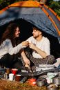 Cheerful couple of travelers with coffee talking in tent