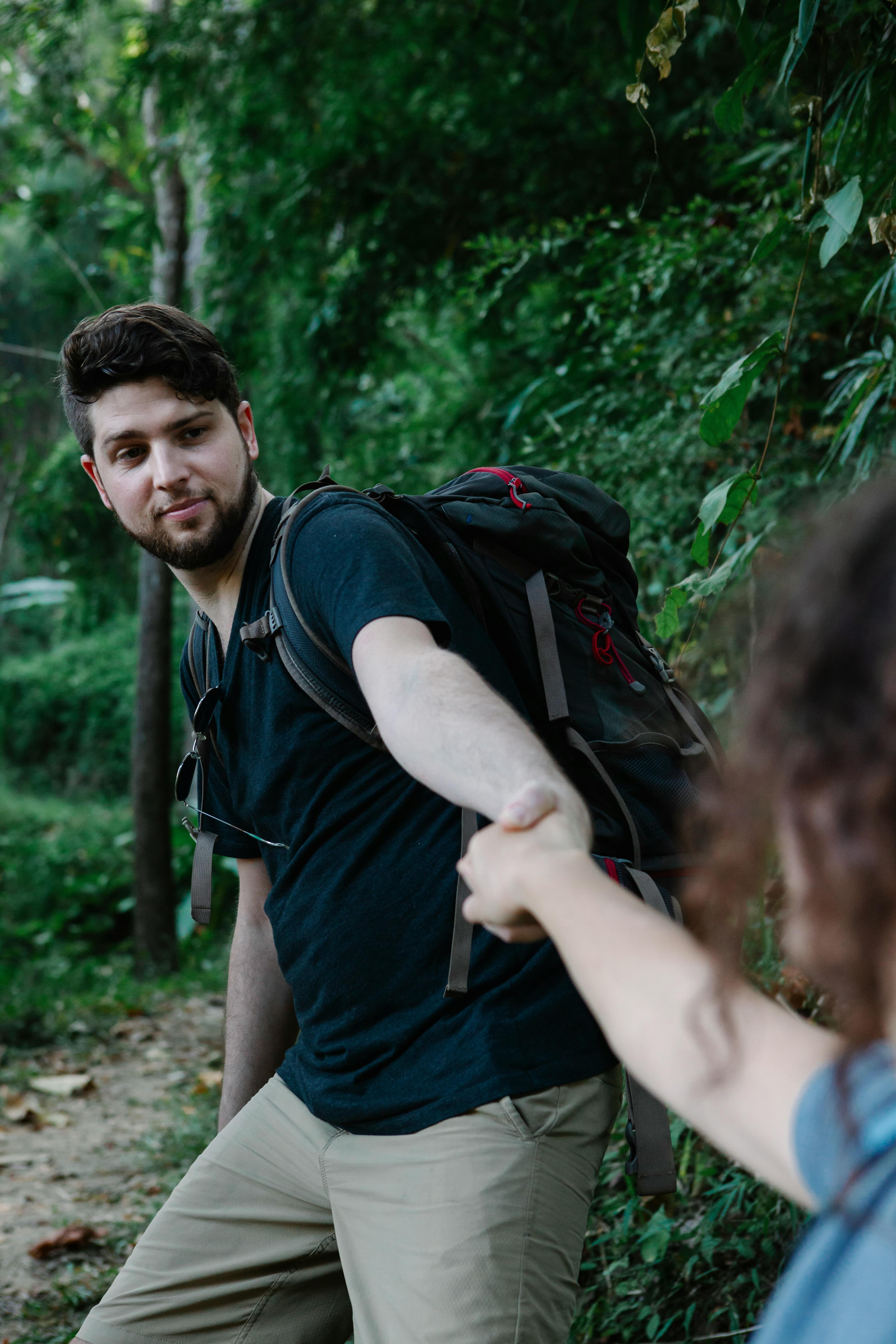 backpacker holding hand of crop beloved in forest