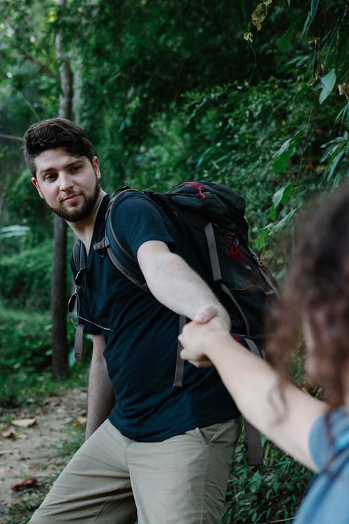 Backpacker holding hand of crop beloved in forest