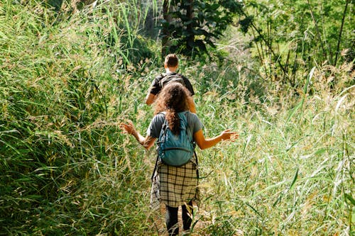 Back view of unrecognizable couple of tourists walking on narrow pathway between bright grass in back lit