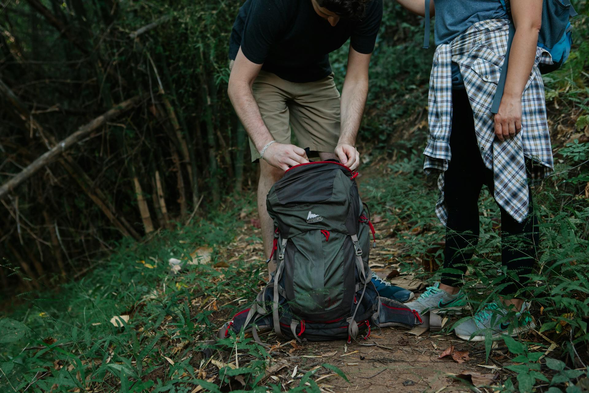 Crop anonymous travelers with rucksack on narrow path in green forest during summer trip