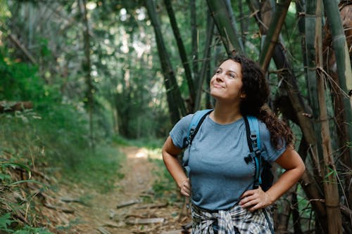 Positive young female traveler admiring nature standing on path in forest