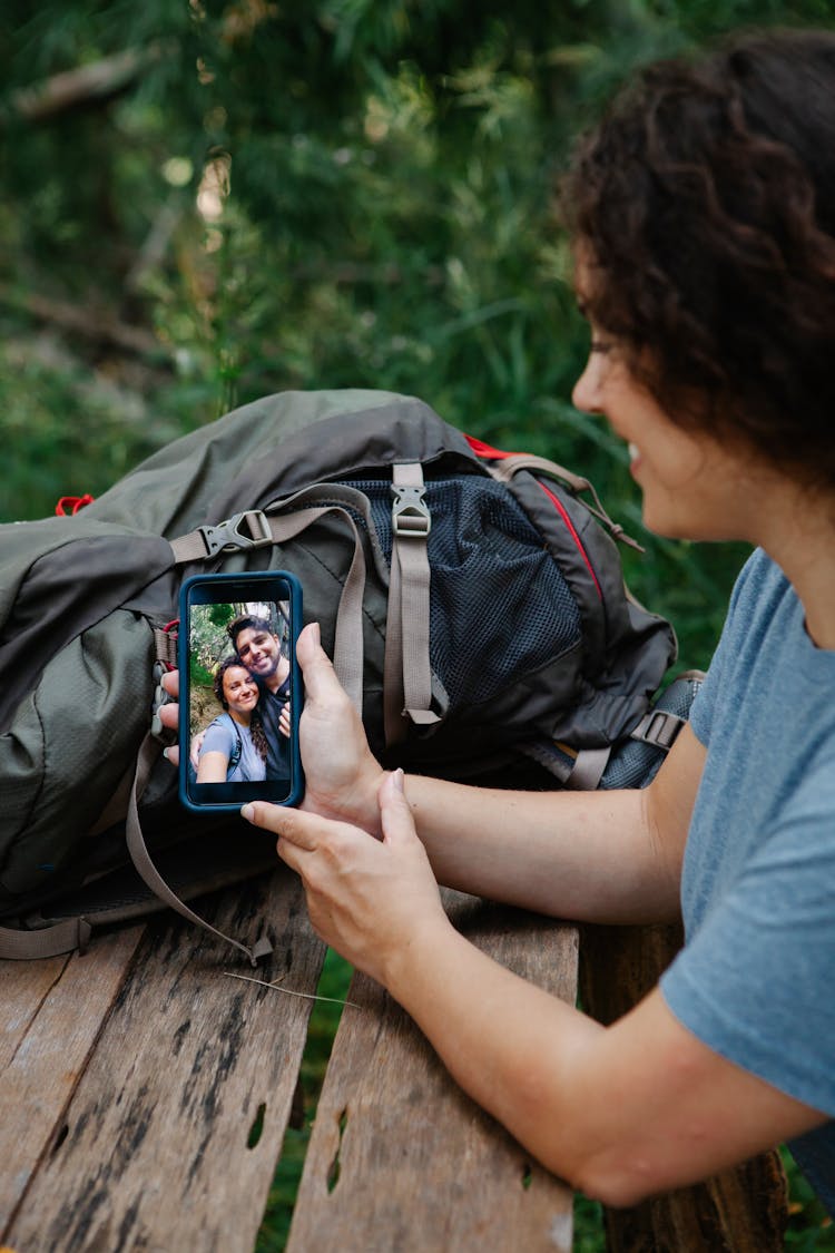 Smiling Young Woman Watching Photo On Smartphone In Lush Green Forest