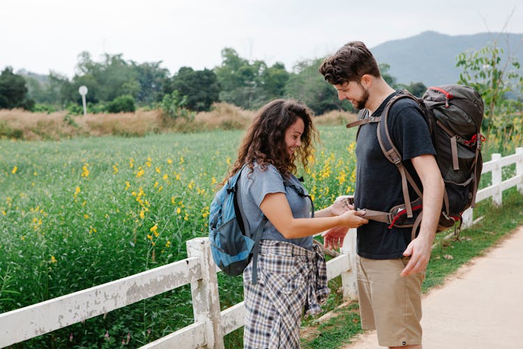 Happy Couple Fastening Backpack Strap During Trip In Countryside