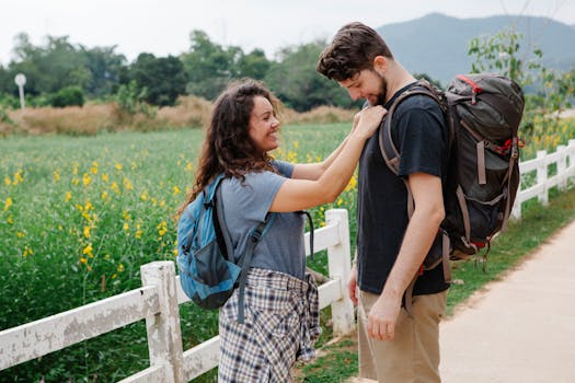 A happy couple with backpacks enjoys a hiking trail through scenic green fields and wildflowers.