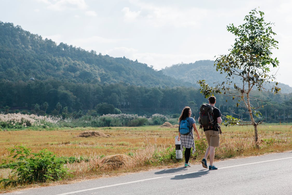 Anonymous couple of tourists walking on road near grassy meadow