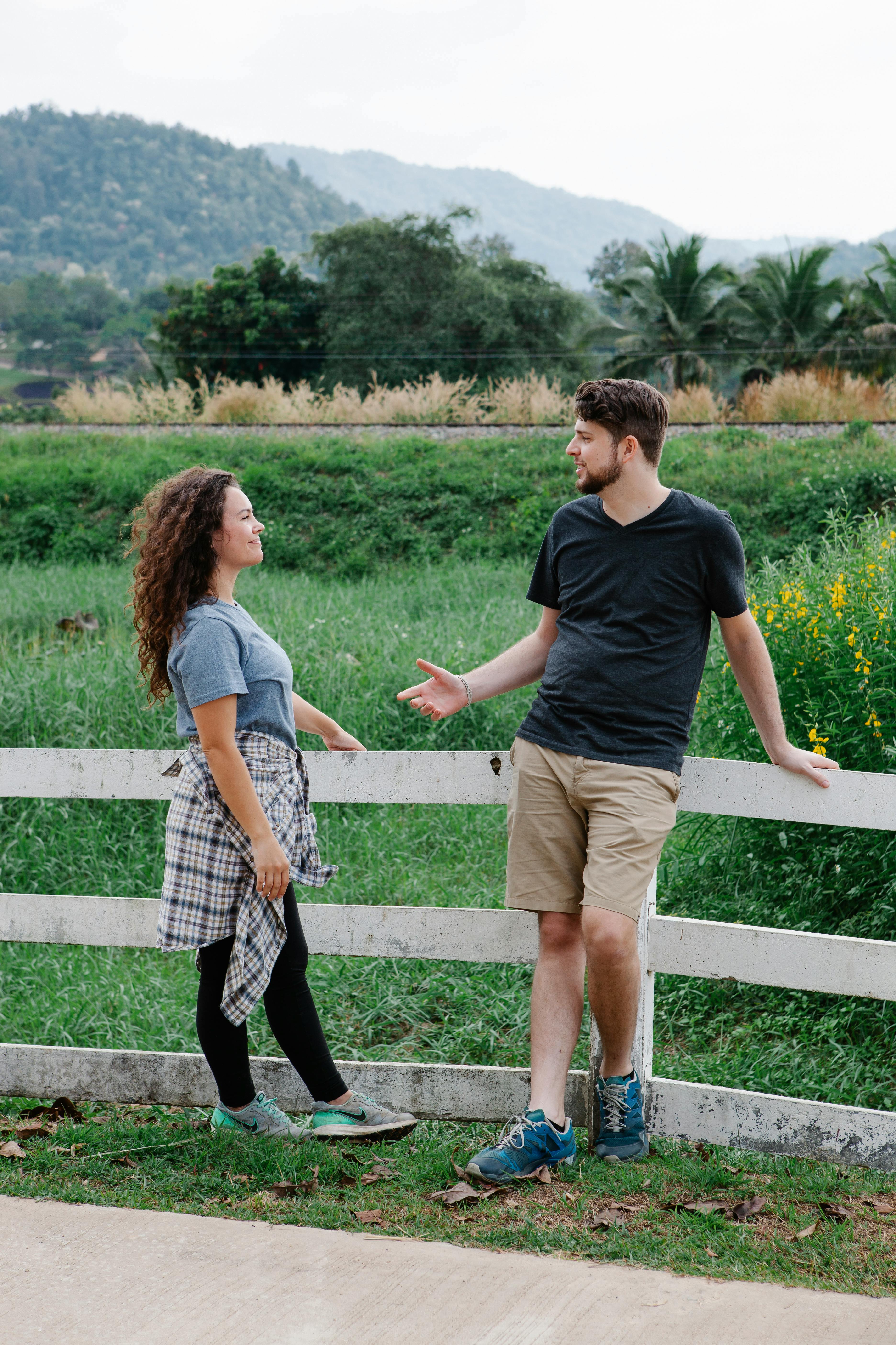 couple standing near wooden fence and communicating in nature