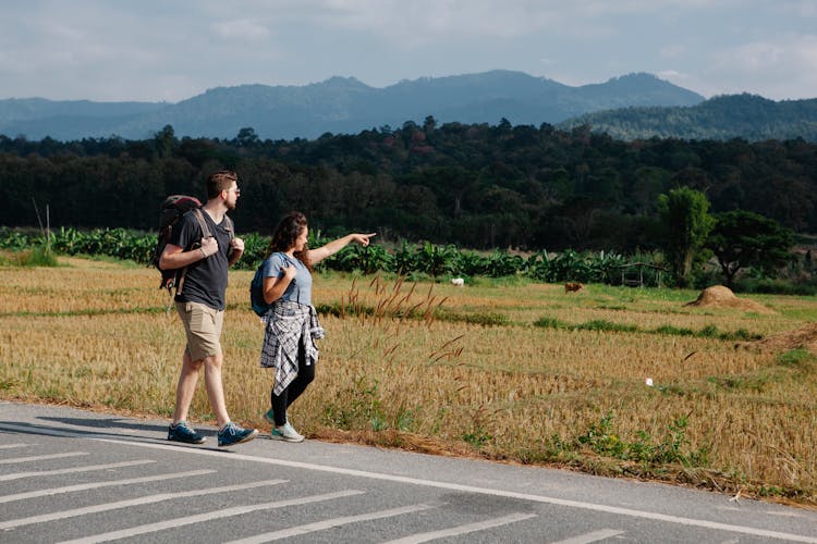 Couple Of Travelers Walking Along Road In Countryside During Trip