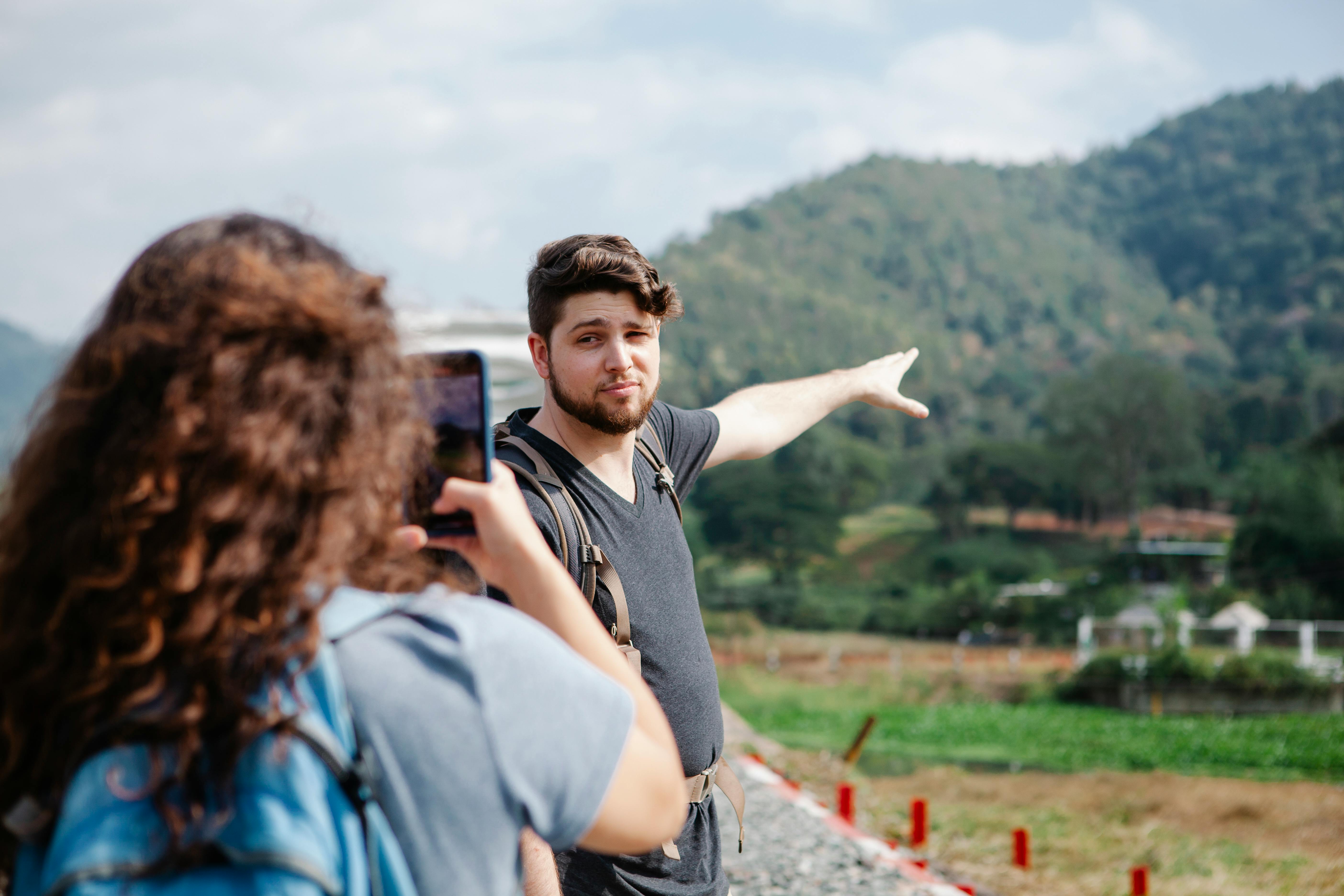 female taking photo of traveler pointing at green hill in countryside