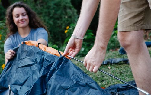 Free Couple of hikers in casual clothes pitching tent together on green grass among plants in nature in daytime Stock Photo